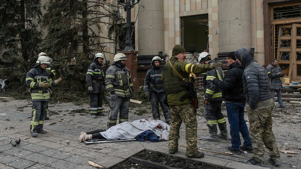 Ukrainian emergency service personnel and servicemen stand around a body of a victim following shelling of the City Hall building in Kharkiv, Ukraine, Tuesday, March 1, 2022. 