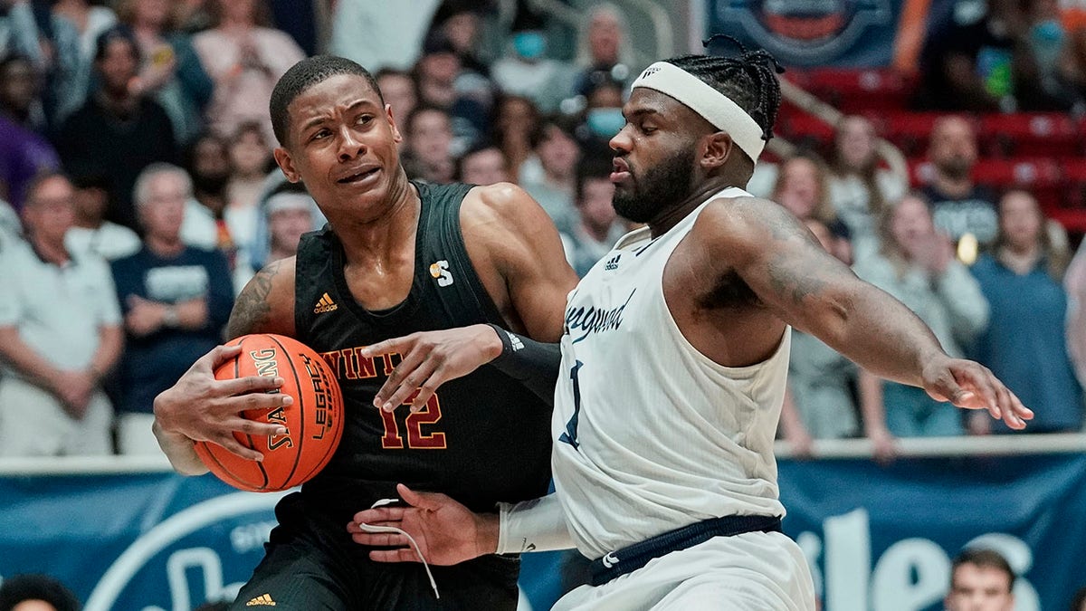 Winthrop forward Cory Hightower (12) drives into the defense of Longwood guard Isaiah Wilkins (1) during the first half of an NCAA college basketball game for the championship of the Big South Conference men's tournament on Sunday, March 6, 2022, in Charlotte, N.C.