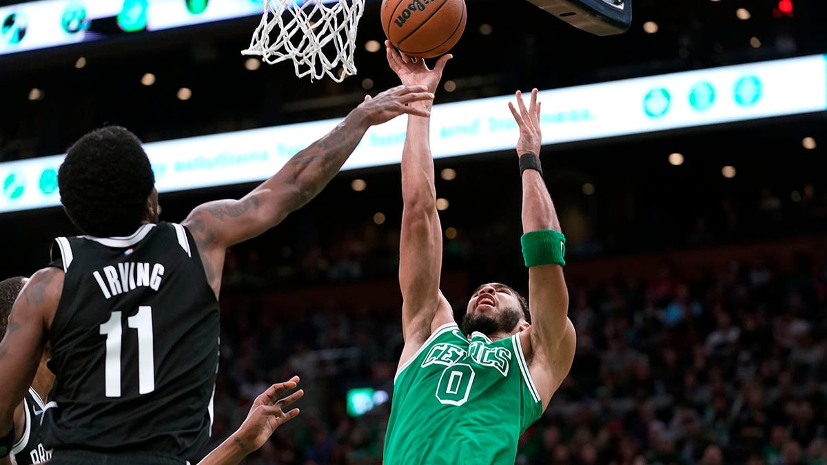 Boston Celtics forward Jayson Tatum (0) shoots as Brooklyn Nets guard Kyrie Irving (11) defends in the first half of an NBA basketball game, Sunday, March 6, 2022, in Boston.