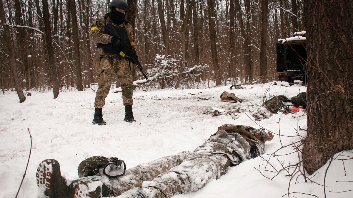 A volunteer of the Ukrainian Territorial Defense Forces looks at a dead body of a soldier lying in a forest in the outskirts of Kharkiv, Ukraine's second-largest city, Monday, March 7, 2022. 