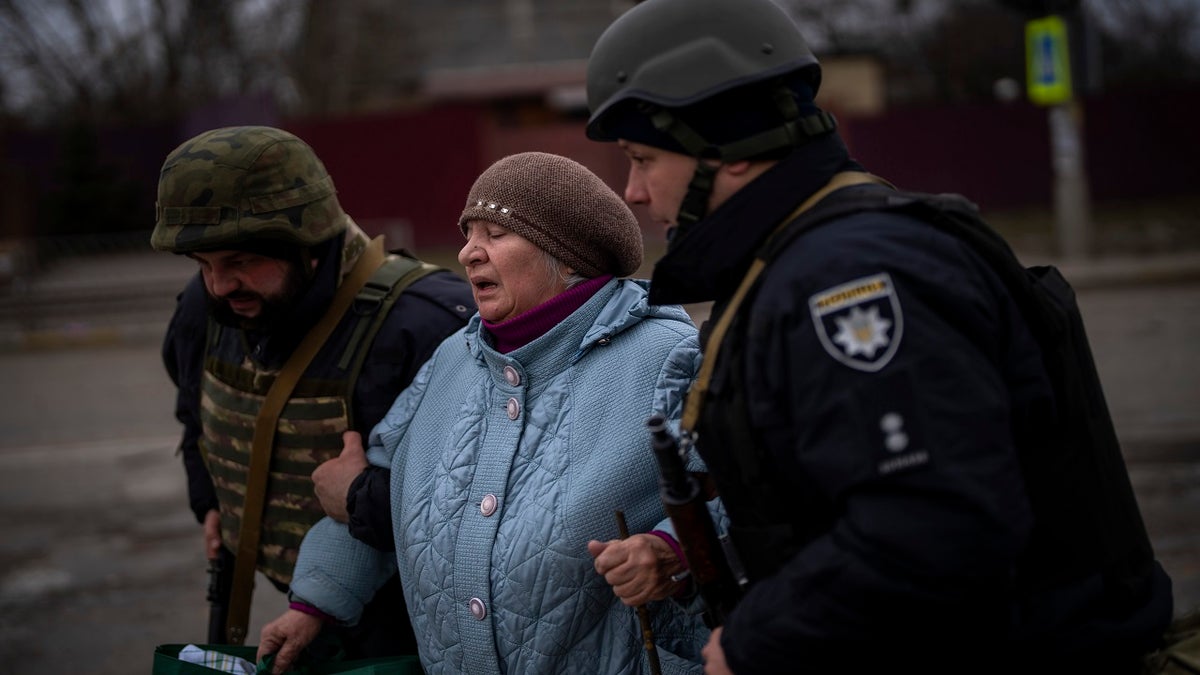 Ukrainian military men help an elderly woman