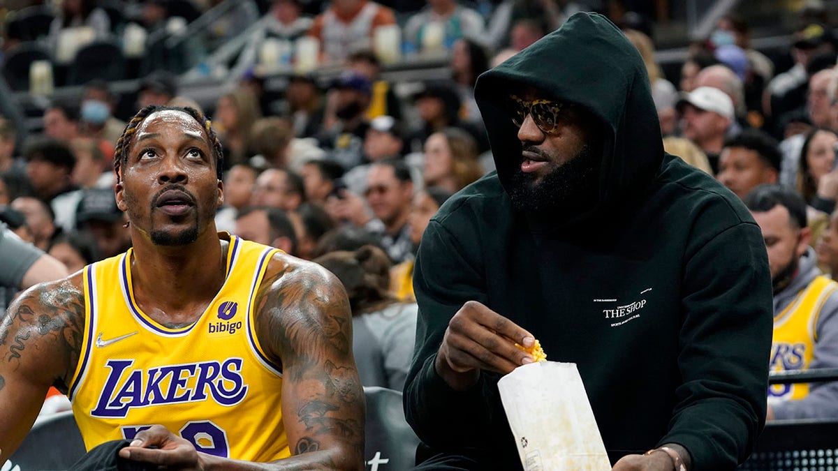 Los Angeles Lakers forward LeBron James, right, talks with teammate Dwight Howard, left, and eats a snack while on the bench during the first half of an NBA basketball game against the San Antonio Spurs, Monday, March 7, 2022, in San Antonio. James did not play.