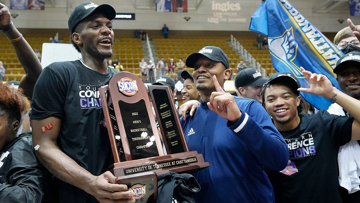 Chattanooga forward Silvio De Sousa, left, and head coach Lamont Paris hold the championship trophy to celebrate their win over Furman in an NCAA college basketball championship game for the Southern Conference tournament, Monday, March 7, 2022, in Asheville, N.C.