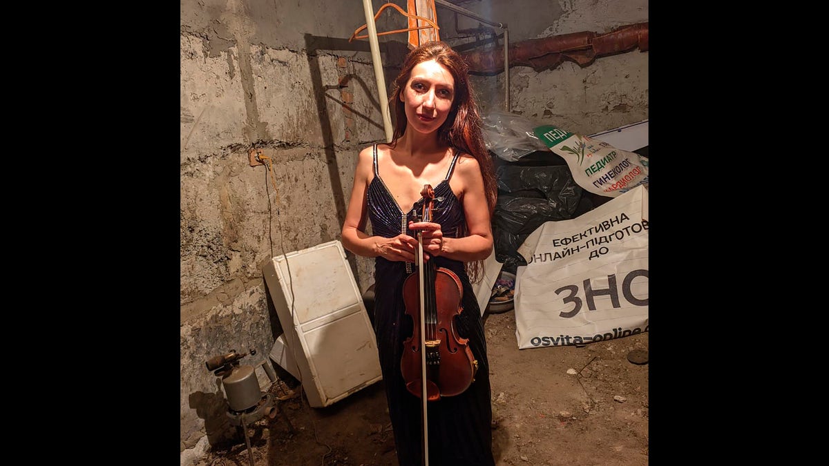 Vera Lytovchenko holds her violin as she poses for a photo in a basement of an apartment building in Kharkiv, Ukraine
