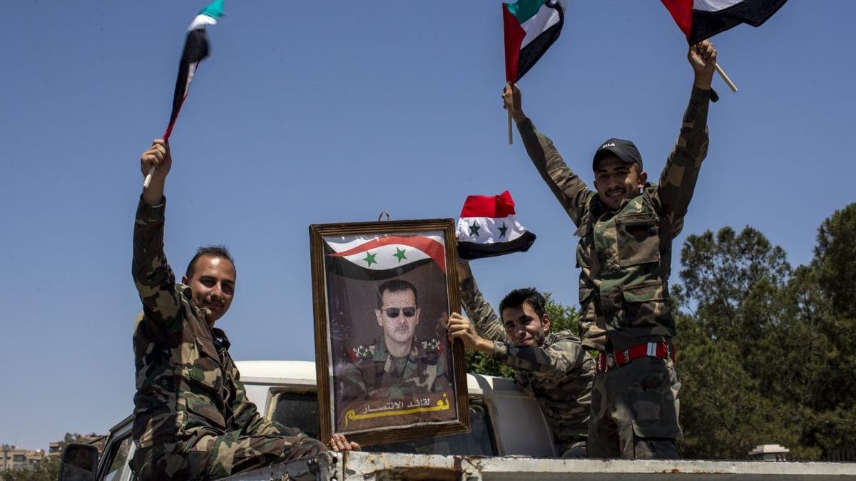FILE - Syrian soldiers hold up Baath party flags and a portrait of Syrian President Bashar Assad. With its war on Ukraine now in its third week, Russian President Vladimir Putin on Friday, March 11, 2022, approved bringing in volunteer fighters from the Middle East into the conflict. 