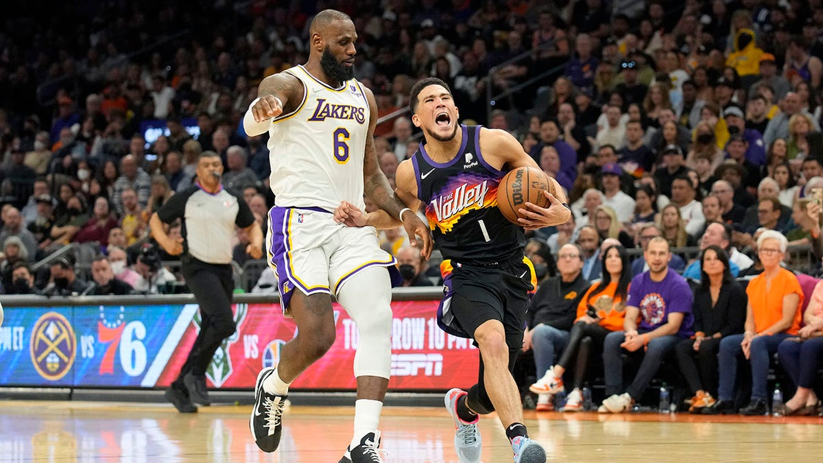 Phoenix Suns guard Devin Booker (1) is pressured by Los Angeles Lakers forward LeBron James during the second half of an NBA basketball game, Sunday, March 13, 2022, in Phoenix.