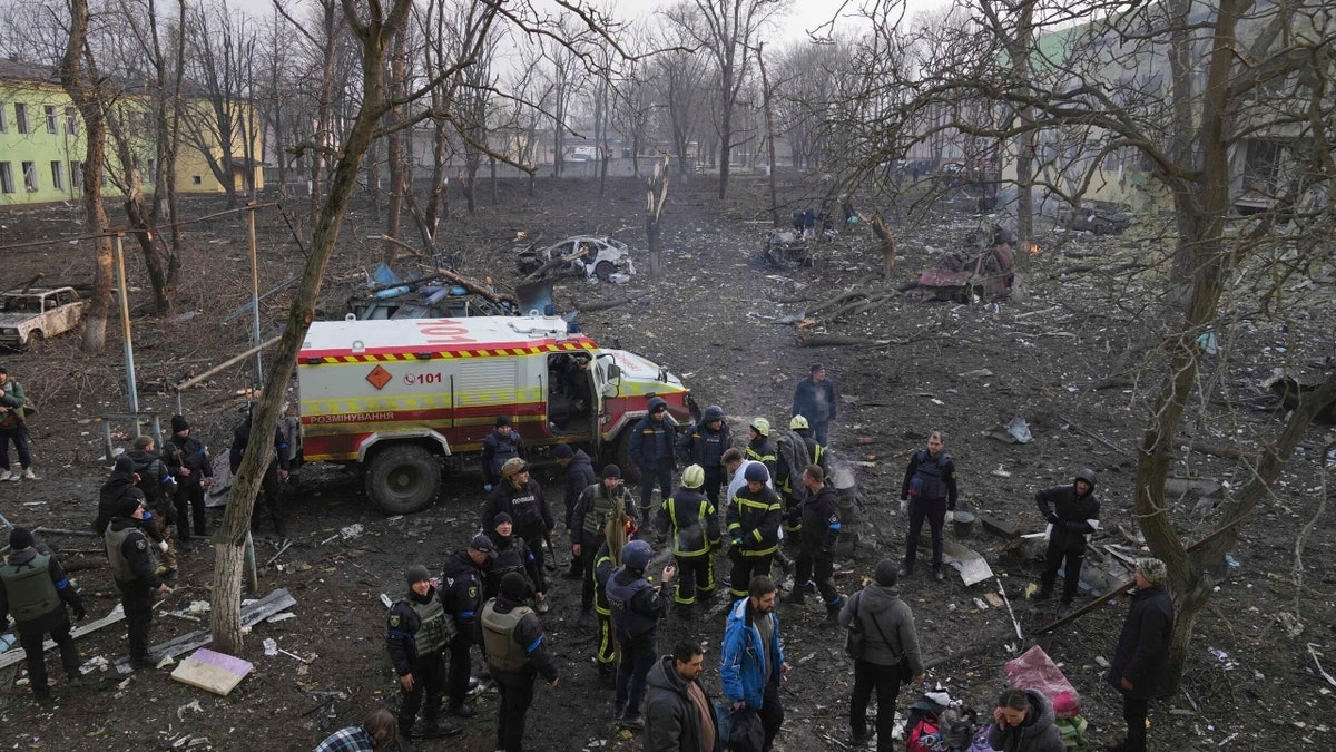 Ukrainian servicemen and firefighters stand in the area outside of a maternity hospital damaged in a shelling attack in Mariupol, Ukraine, Wednesday, March 9, 2022. Associated Press journalists, who have been reporting from inside blockaded Mariupol since early in the war, documented this attack on the hospital and saw the victims and damage firsthand. They shot video and photos of several bloodstained, pregnant mothers fleeing the blown-out maternity ward, medics shouting, children crying. (AP Photo/Evgeniy Maloletka)