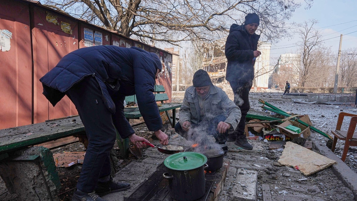 Men cook a meal in a street in Mariupol, Ukraine, Sunday, March 13, 2022. The surrounded southern city of Mariupol, where the war has produced some of the greatest human suffering, remained cut off despite earlier talks on creating aid or evacuation convoys. (AP Photo/Evgeniy Maloletka)