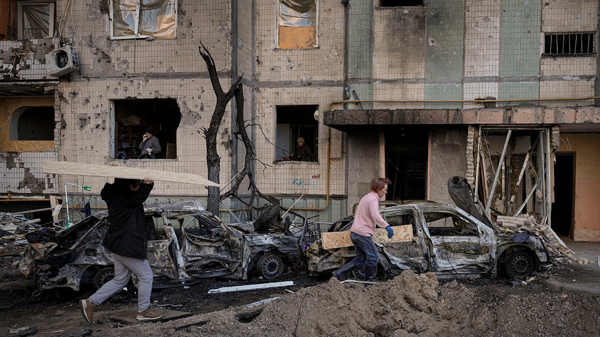 People carry wooden boards to cover the windows of a building damaged by a bombing the previous day in Kyiv, Ukraine, Monday, March 21, 2022.