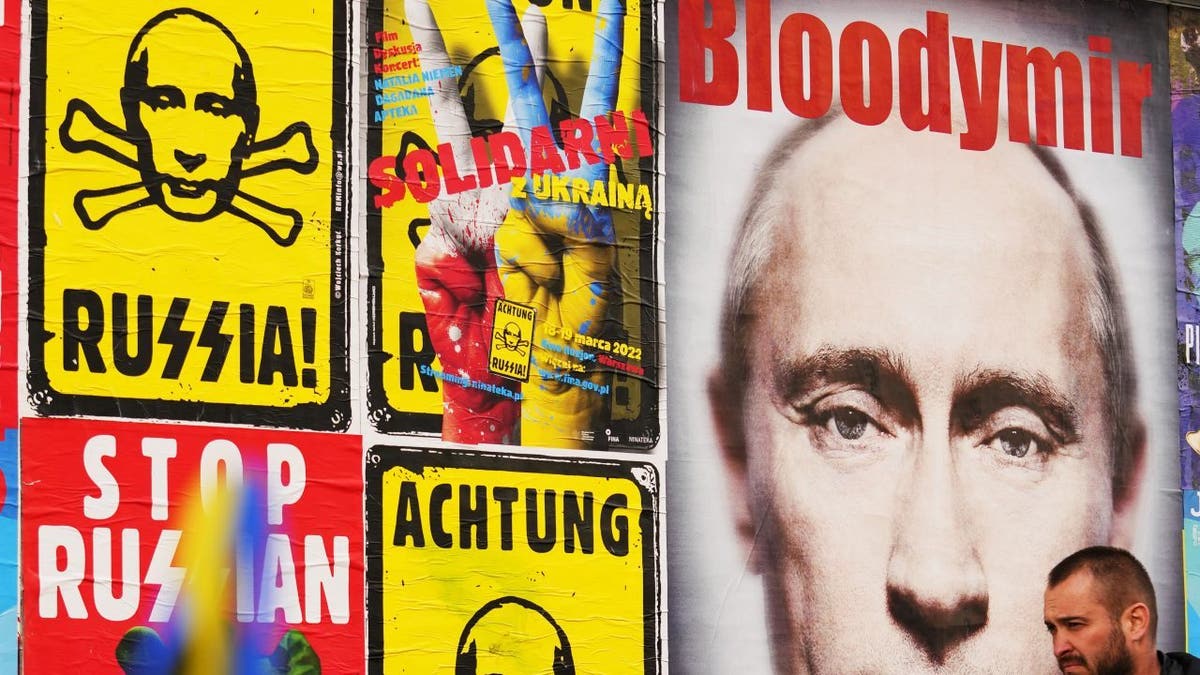 A man walks past a wall with posters depicting Russian President Vladimir Putin in Warsaw, Poland, on Thursday, March 24, 2022. 