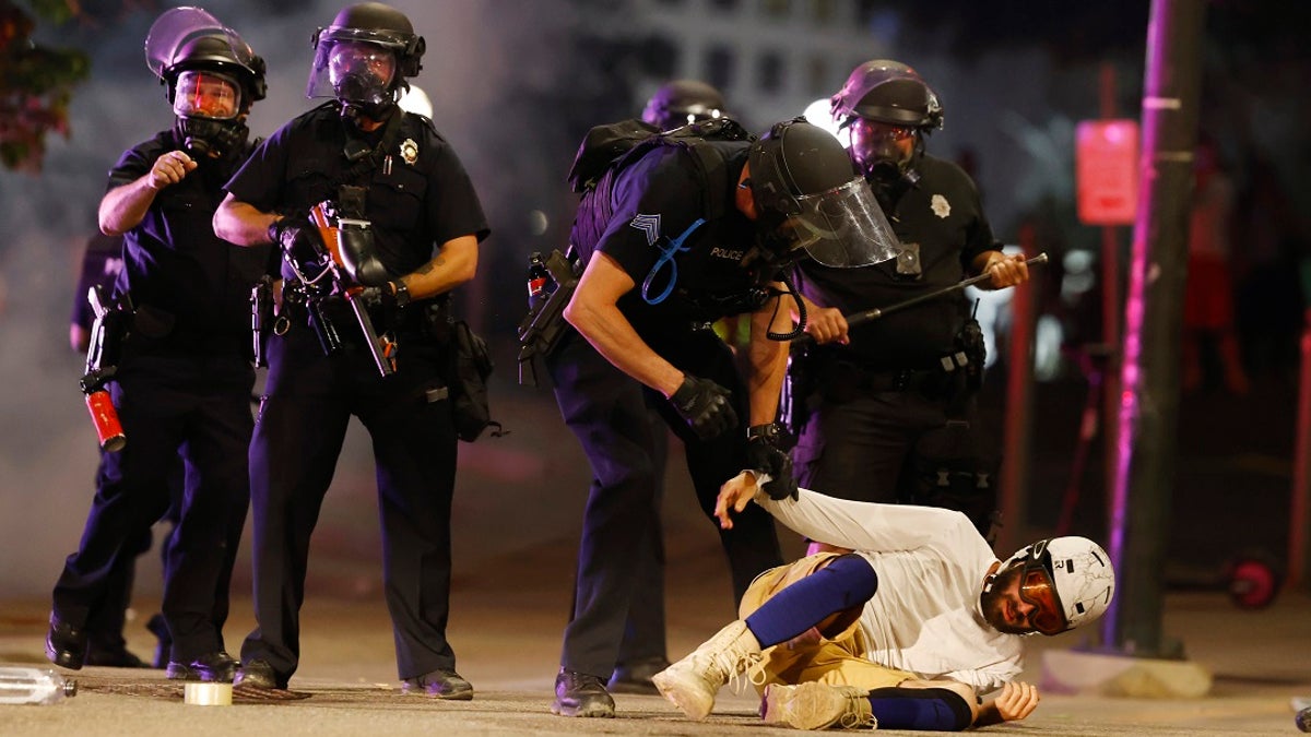 Denver Police Department officers clear a man who fell to the street after they used tear gas and rubber bullets to disperse a protest outside the State Capitol over the death of George Floyd on May 28, 2020, in Denver.