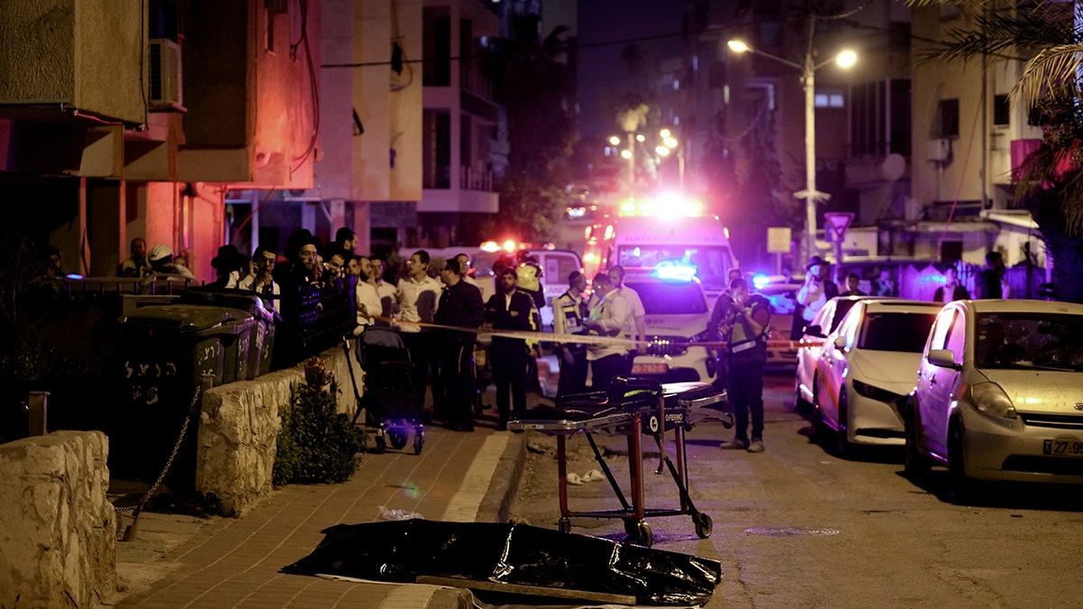 Ultra-Orthodox Jews stand near the covered body of a shooting victim in Bnei Brak, Israel, Tuesday, March 29, 2022.
