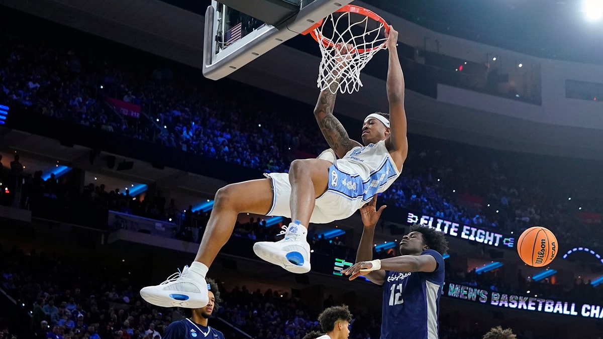 North Carolina's Armando Bacot, left, hangs on the rim after a dunk past St. Peter's Clarence Rupert during the first half of a college basketball game in the Elite 8 round of the NCAA tournament, Sunday, March 27, 2022, in Philadelphia. 