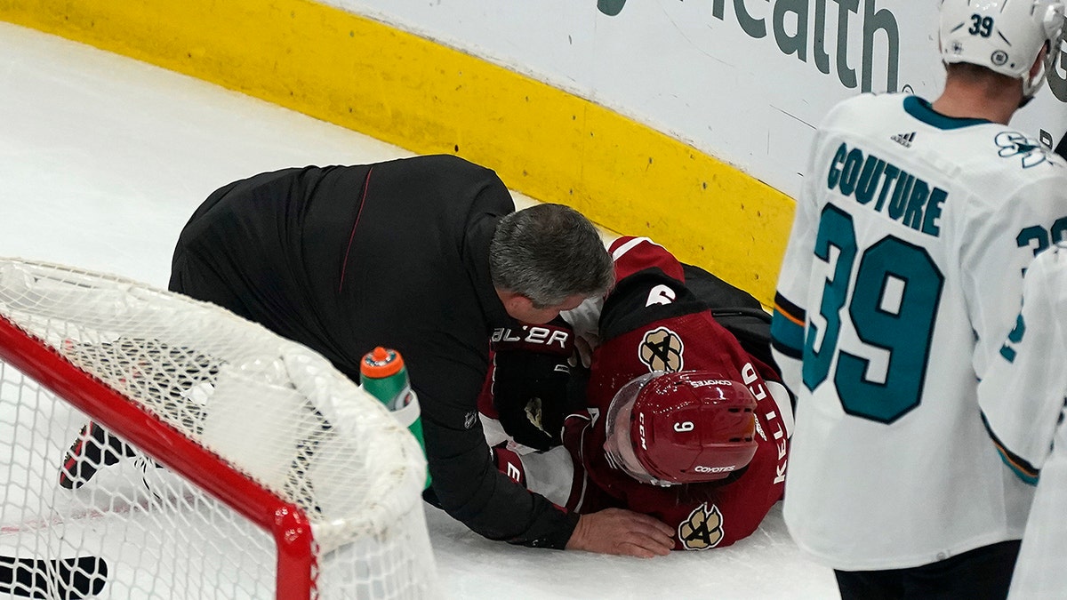 A trainer attends to Arizona Coyotes' Clayton Keller (9), who collided against the boards during the third period of the team's NHL hockey game against the San Jose Sharks, Wednesday, March 30, 2022, in Glendale, Arizona.