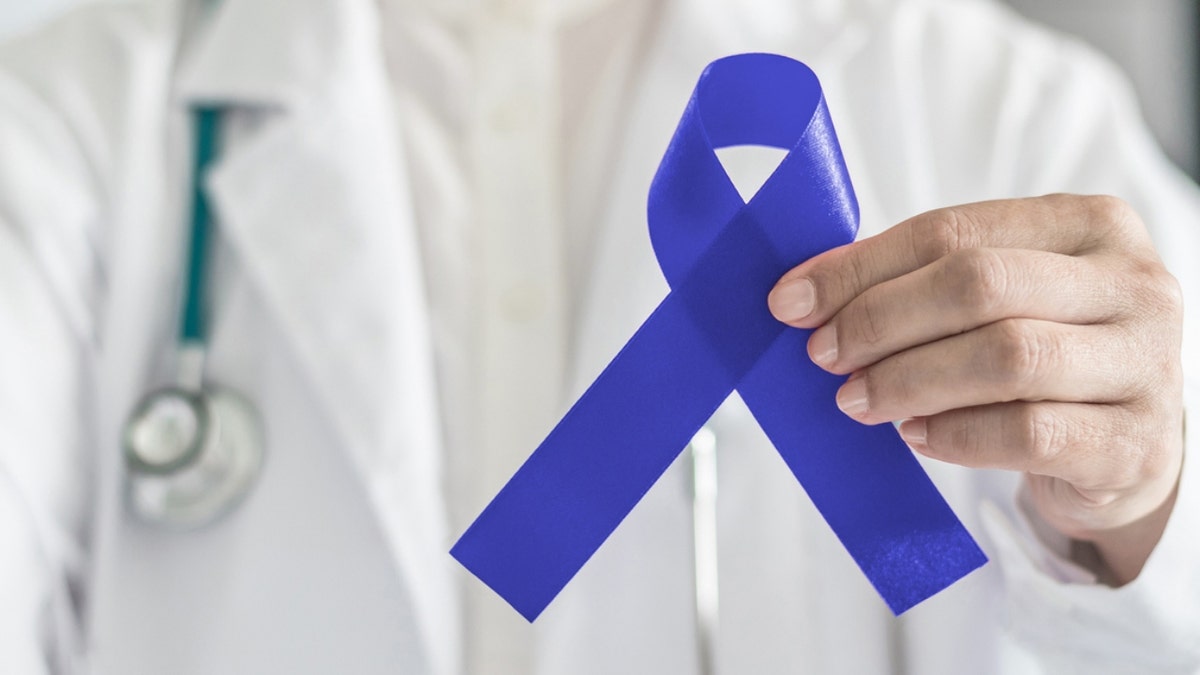 A doctor holding a dark blue ribbon for colon cancer