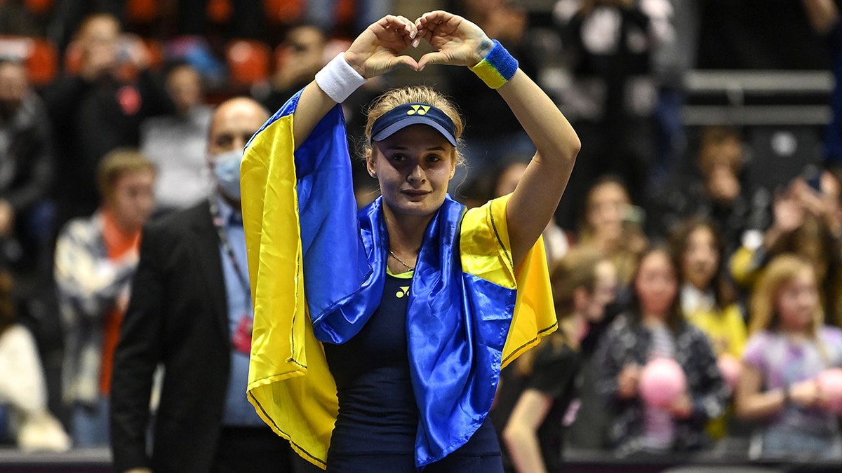 Ukraine's Dayana Yastremska, wrapped in the Ukrainian national flag, reacts at the end of the WTA 6eme Sens Open semi-final tennis match against Romania's Sorana Cirstea in Lyon, on March 5, 2022.