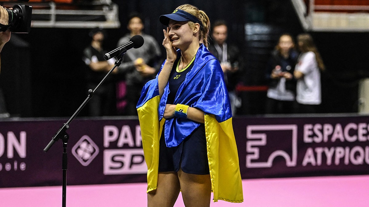 Ukraine's Dayana Yastremska, wrapped in the Ukrainian national flag, reacts at the end of the WTA 6eme Sens Open semi-final tennis match against Romania's Sorana Cirstea in Lyon, on March 5, 2022.