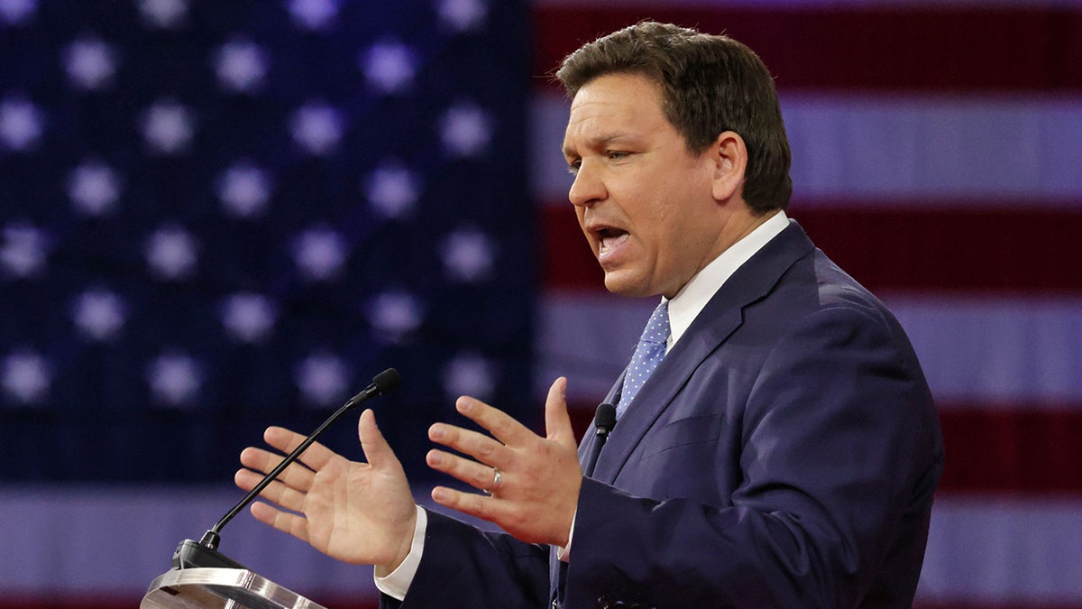 Florida Gov. Ron DeSantis speaks in a blue suit in front of an American flag