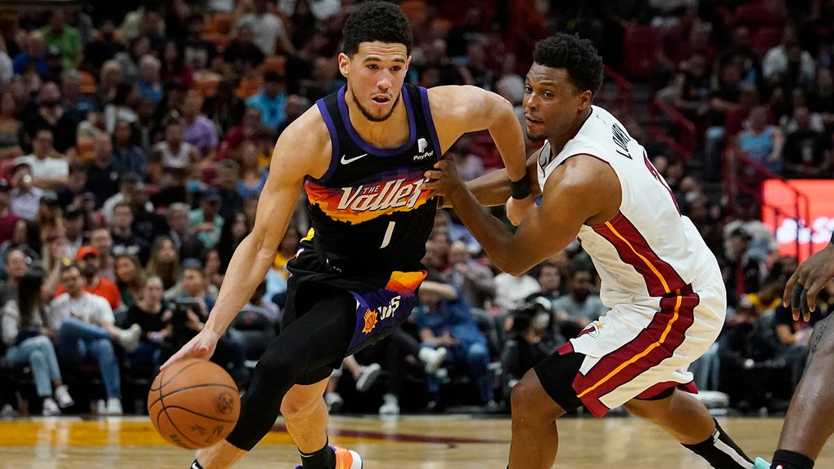 Phoenix Suns guard Devin Booker (1) gets away from Miami Heat guard Kyle Lowry (7) during the first half of an NBA basketball game, Wednesday, March 9, 2022, in Miami.