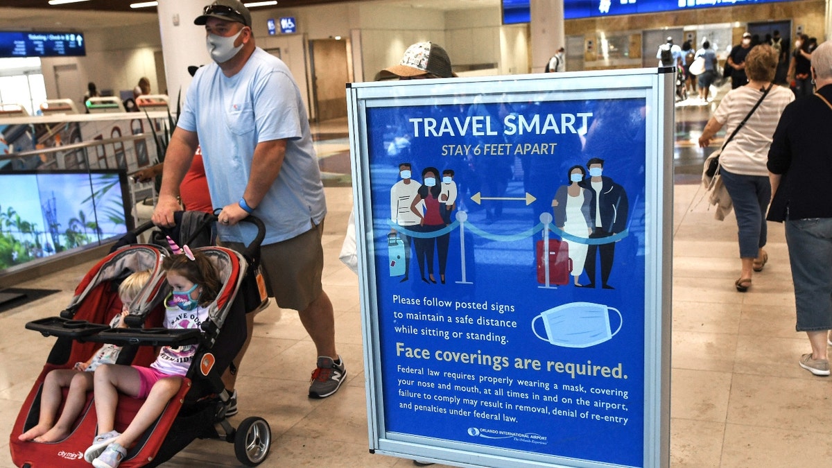 ORLANDO, FLORIDA, UNITED STATES - 2021/05/01: Travelers wearing face masks as a preventive measure against the spread of covid-19 walk by a sign advising of the requirements for social distancing and the wearing of face coverings at Orlando International Airport. On April 30, 2021, the Transportation Security Administration extended the federal mask mandate, which was set to expire on May 11, until September 13 for all air passengers over the age of 2. (Photo by Paul Hennessy/SOPA Images/LightRocket via Getty Images)