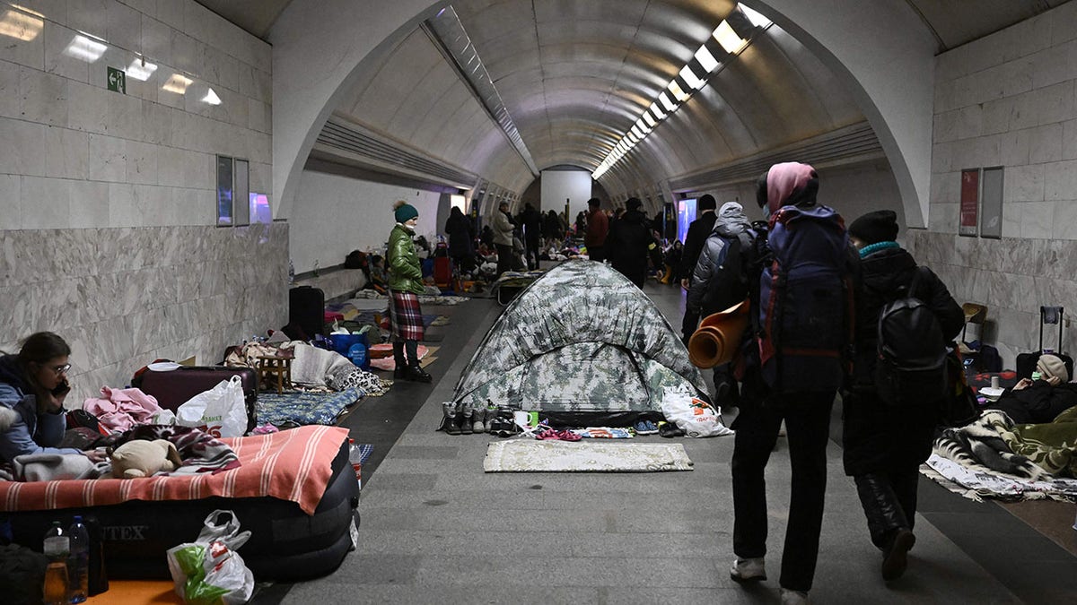 TOPSHOT - Civilians walk by Ukraine residents who use an underground metro station as bomb shelter in Kyiv on March 2, 2022. - On the seventh day of fighting in Ukraine Russia claims control on March 2, 2022 of the southern port city of Kherson, street battles rage in Ukraine's second-biggest city Kharkiv, and Kyiv braces for a feared Russian assault. (Photo by Aris Messinis / STF / AFP) 