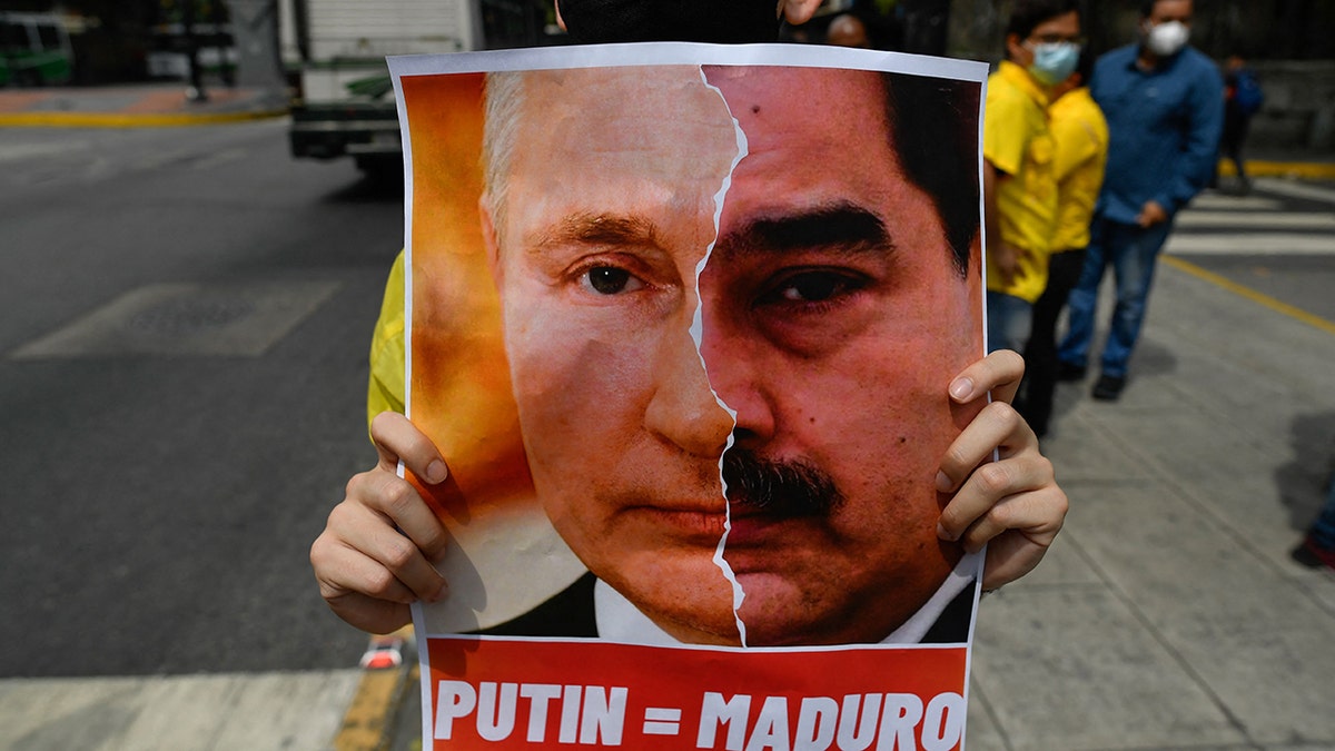 An activist member of opposition party Primero Justicia holds a placard showing the face of Russian President Vladimir Putin and Venezuelan President Nicolas Maduro during a protest against the Russian invasion in Ukraine, in Caracas on March 4, 2022. 