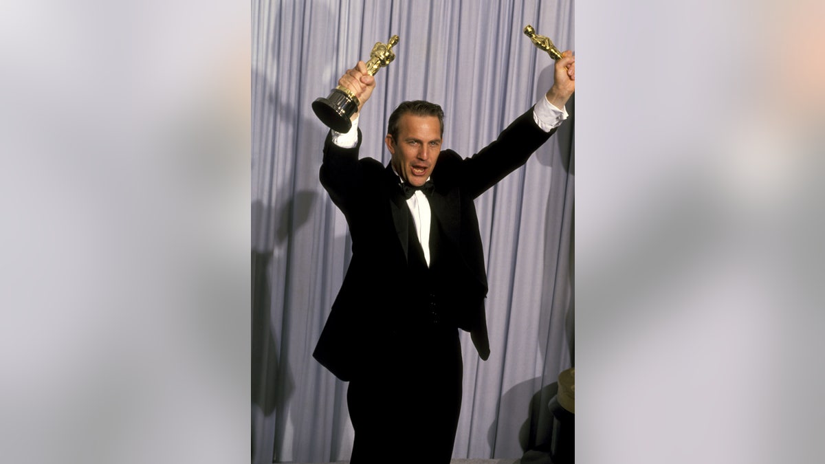 Dances with Wolves director Kevin Costner holds Oscars in the air after winning Academy awards