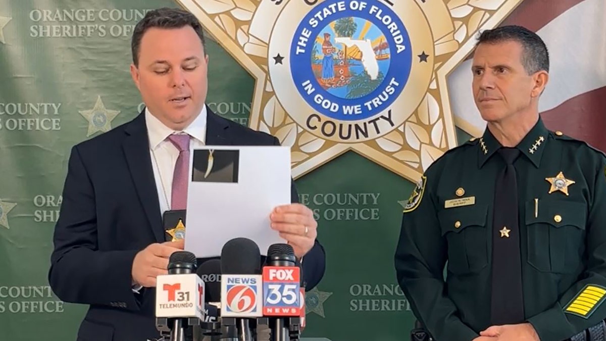 Joe Covelli, a Homicide Sergeant at the Orange County Sheriff's Office holds up a picture of the necklace during a press conference on Thursday.