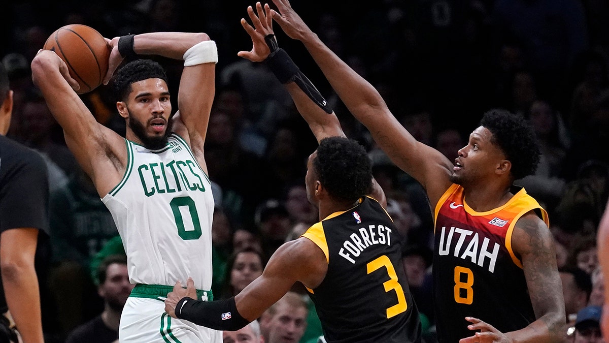 Boston Celtics forward Jayson Tatum (0) looks to pass while covered by Utah Jazz guard Trent Forrest (3) and forward Rudy Gay (8) during the first half of an NBA basketball game Wednesday, March 23, 2022, in Boston.