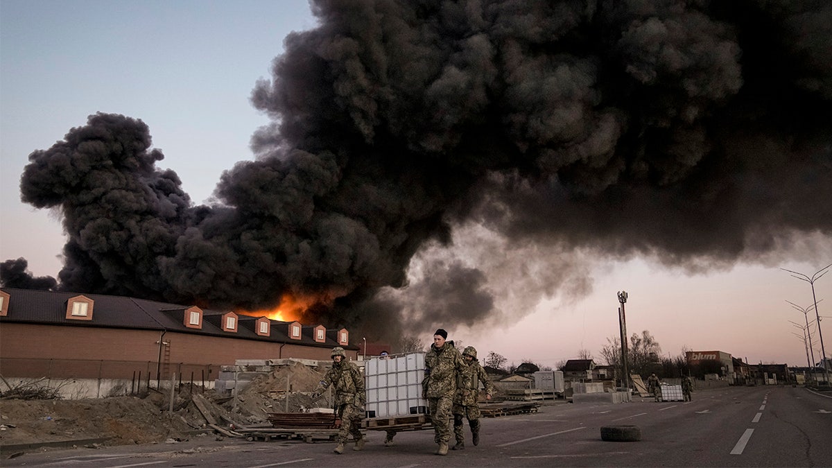 Ukrainian service members carry containers backdropped by a blaze at a warehouse after a bombing on the outskirts of Kyiv, Ukraine, Thursday, March 17, 2022.