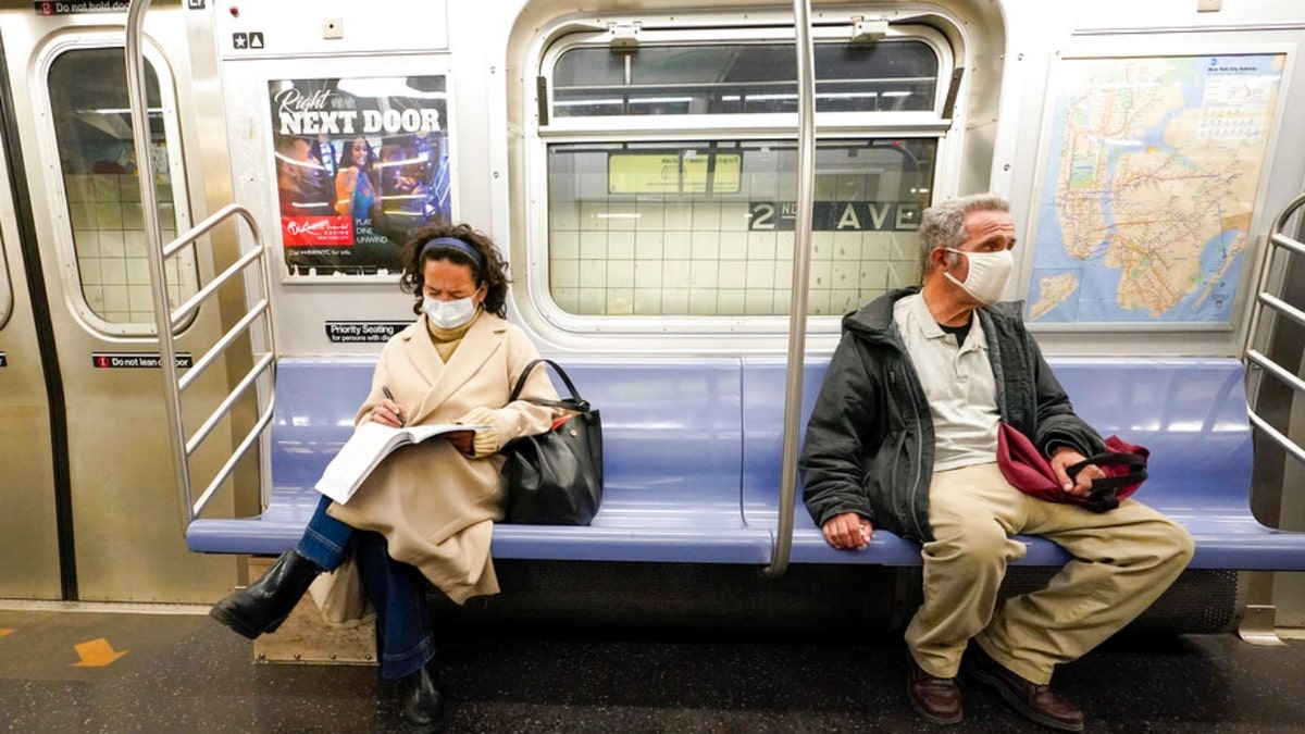 FILE - Commuters wear face masks and social distance while riding an M Train, Tuesday, March 9, 2021, in New York's subway system.