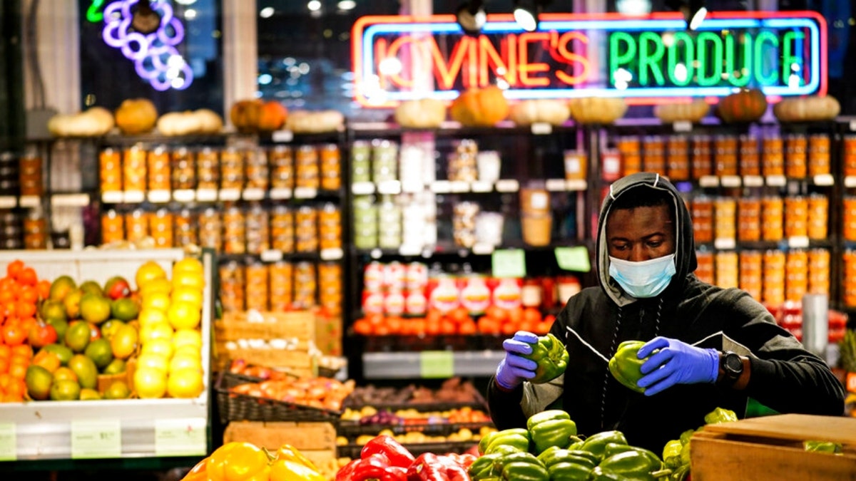 A grocer wearing a protective mask as a precaution against the spread of the coronavirus stocks papers at the Reading Terminal Market in Philadelphia, Wednesday, Feb. 16, 2022.