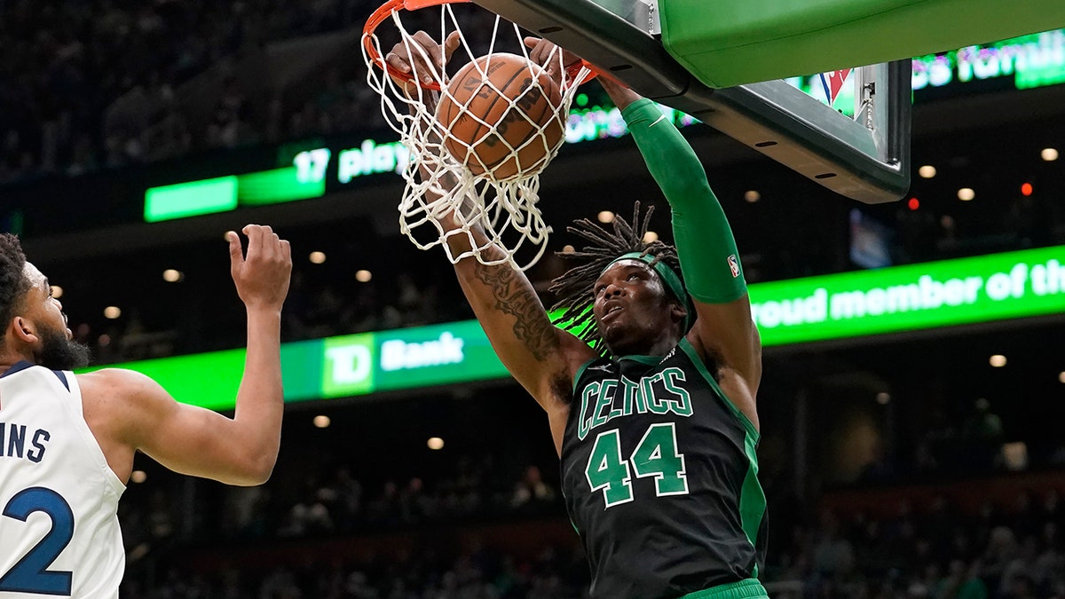 Boston Celtics center Robert Williams III (44) sinks the ball as Minnesota Timberwolves center Karl-Anthony Towns (32), left, tries to defend in the first half of an NBA basketball game, Sunday, March 27, 2022, in Boston.