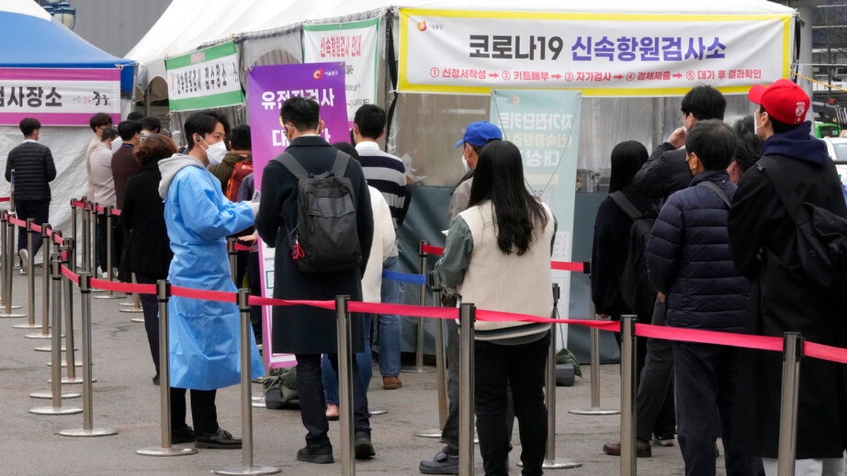 A medical worker guides people waiting for a coronavirus test at a makeshift testing site in Seoul, South Korea, Thursday, March 17, 2022. 