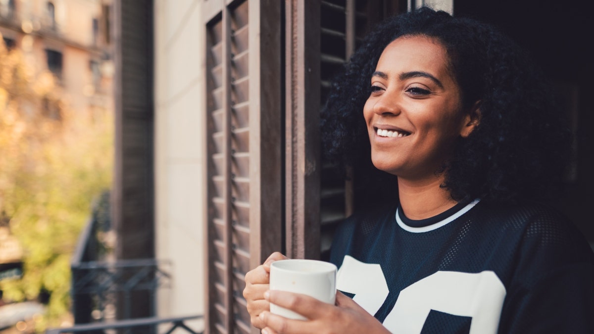 A woman smiles and holds a cup of coffee.
