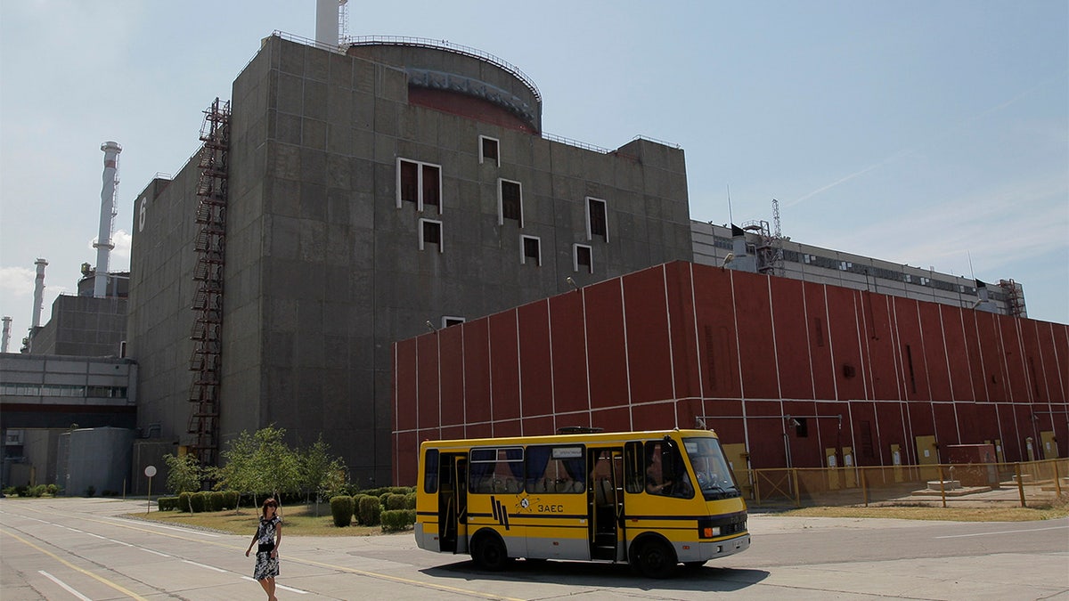 a yellow bus parks in front of an imposing brick building, part of the Zaporizhzhya nuclear power plant