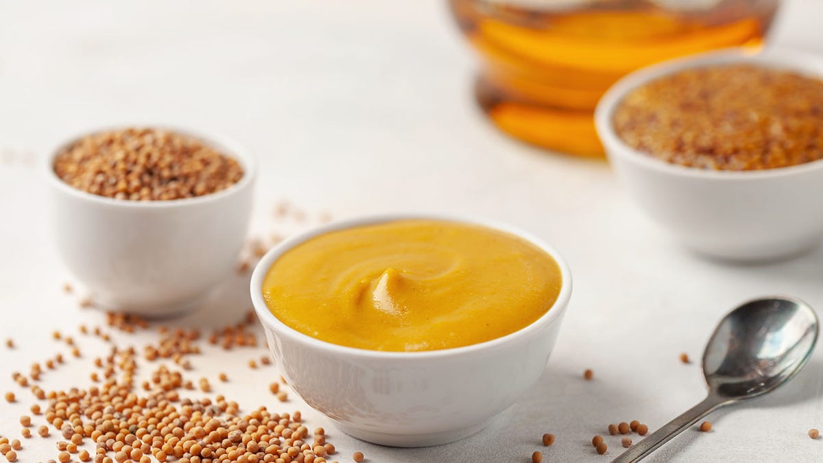 Mustard sauce in a bowl and seeds on a bright background.