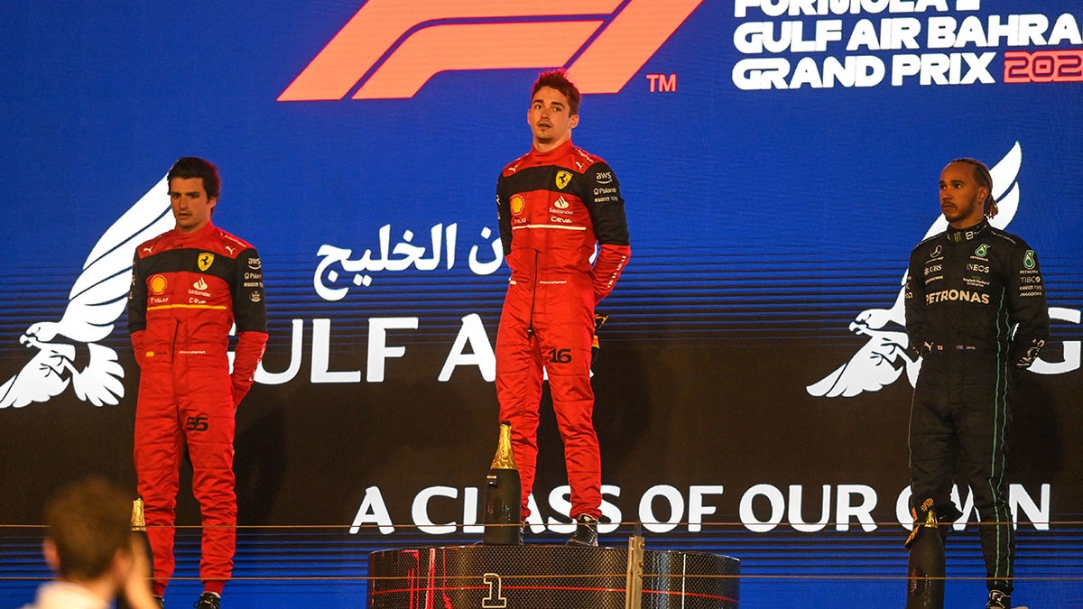 Ferrari's Spanish driver Carlos Sainz Jr (L), Ferrari's Monegasque driver Charles Leclerc (C) and Mercedes' British driver Lewis Hamilton stand for the national anthem on the podium after the Bahrain Formula One Grand Prix at the Bahrain International Circuit in the city of Sakhir on March 20, 2022. (Photo by OZAN KOSE / AFP) (Photo by OZAN KOSE/AFP via Getty Images)