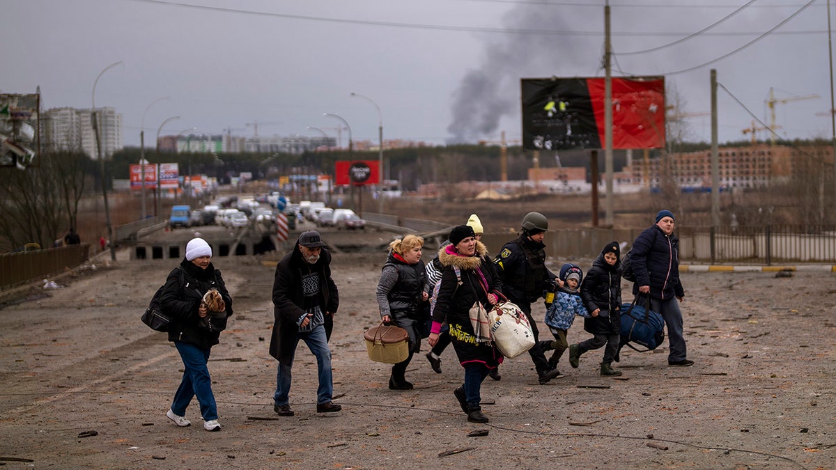 A Ukrainian police officer helps people as artillery echoes nearby while fleeing Irpin in the outskirts of Kyiv, Ukraine, Monday, March 7, 2022. Russia announced yet another cease-fire and a handful of humanitarian corridors to allow civilians to flee Ukraine. Previous such measures have fallen apart and Moscow’s armed forces continued to pummel some Ukrainian cities with rockets Monday. (AP Photo/Emilio Morenatti)