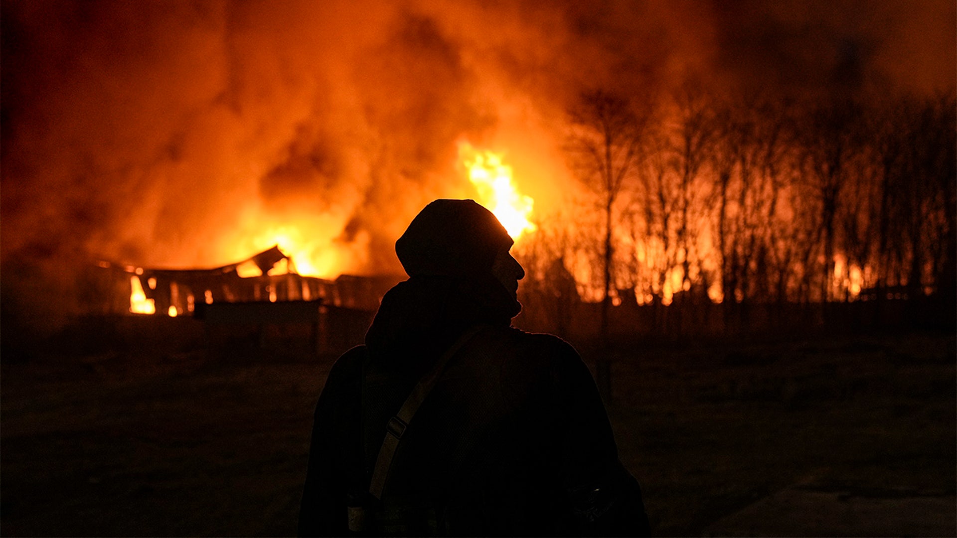 A Ukrainian serviceman is backdropped by a blaze at a warehouse after a bombing on the outskirts of Kyiv, Ukraine, Thursday, March 17, 2022.