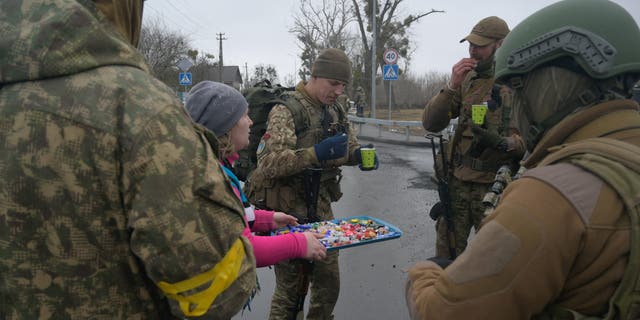 A woman offers sweets to Ukrainian servicemen, as Russia's invasion of Ukraine continues, in the village of Yasnohorodka in the Kyiv region, Ukraine, March 2, 2022. 