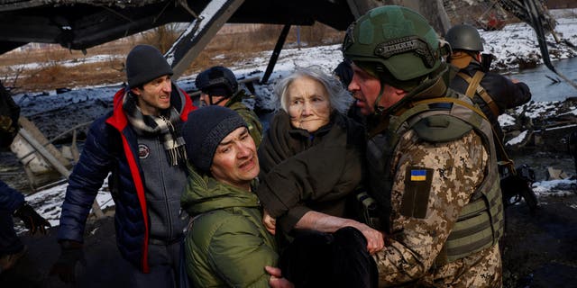 Two men carry a woman as people flee from advancing Russian troops whose attack on Ukraine continues in the town of Irpin outside Kyiv, Ukraine, March 8, 2022. 