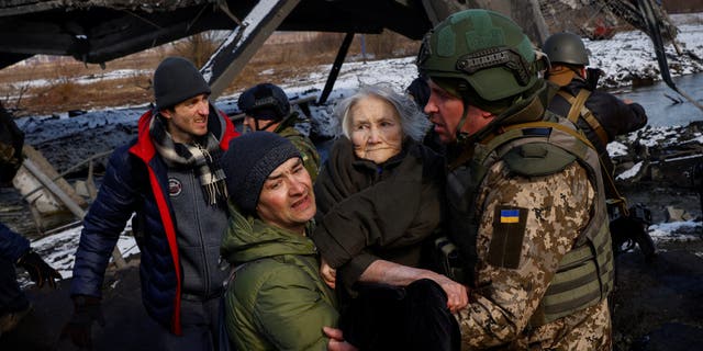 Two men carry a woman as people flee from advancing Russian troops whose attack on Ukraine continues in the town of Irpin outside Kyiv, Ukraine, March 8, 2022.