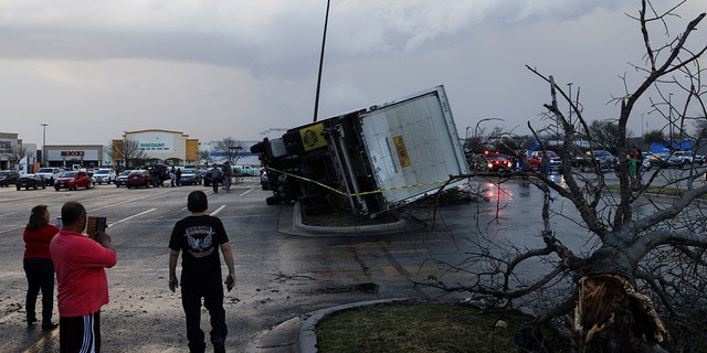 La gente mira un camión volcado en un estacionamiento después de que un tornado en un sistema de tormentas generalizado aterrizó en Round Rock, Texas, EE. UU., el 21 de marzo de 2022.