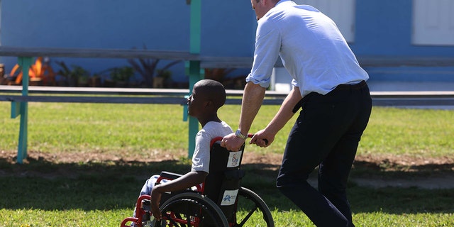 Prince William, Duke of Cambridge pushes a boy in a wheelchair as he visits The Grand Bahama Children's Home on March 26, 2022, in Freeport, Bahamas. 