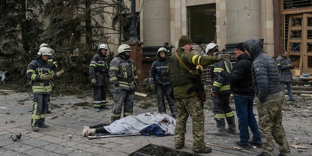 Ukrainian emergency service personnel and servicemen stand by a body of a victim following shelling of the City Hall in Kharkiv, Ukraine, Tuesday, March 1, 2022.