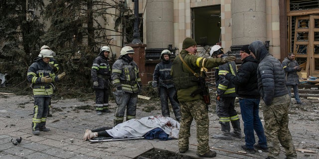 Ukrainian emergency service personnel and servicemen stand by a body of a victim following shelling of the City Hall in Kharkiv, Ukraine, Tuesday, March 1, 2022.