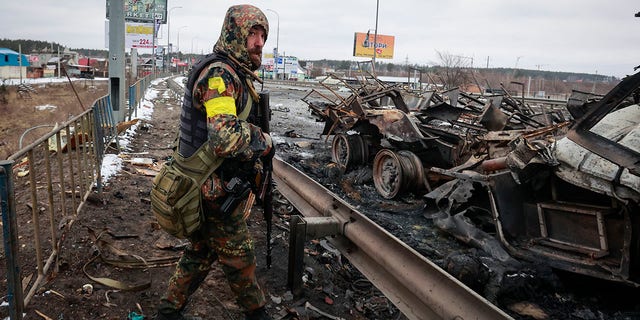 An armed man stands by the remains of a Russian military vehicle in Bucha, close to the capital Kyiv, Ukraine, Tuesday, March 1, 2022. 
