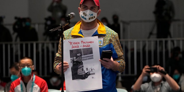 Lee Reaney, a Canadian journalist working for the Kyiv Post, holds a photo of Yevhen Malyshev, a 19-year-old former athlete on Ukraine's junior biathlon team who, according to the International Biathlon Union, died serving the Ukrainian military, as he speaks during a press conference at the 2022 Winter Paralympics in Beijing, Wednesday, March 2, 2022. 