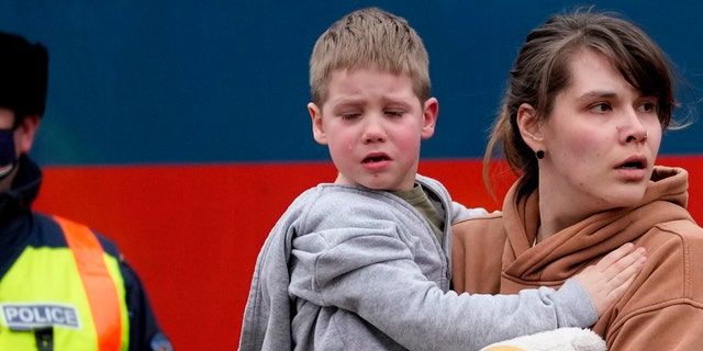 A woman carries a crying child as she arrives at the train station in Zahony, Hungary, on March 5, 2022. (AP Photo/Darko Vojinovic)